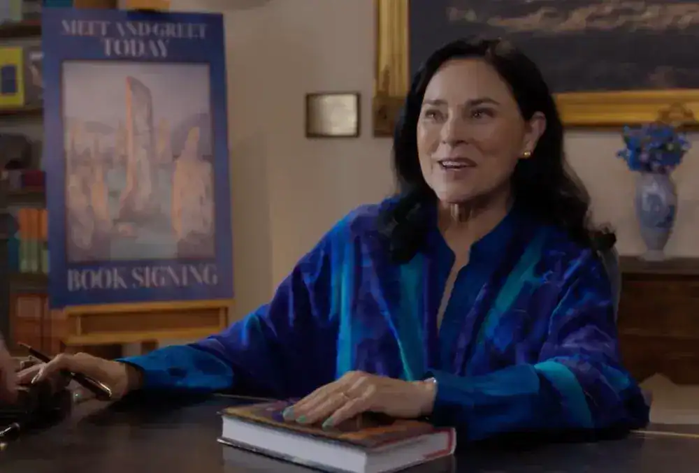 Diana Gabaldon en la escena post-créditos del final de Outlander, firmando libros con camisa azul